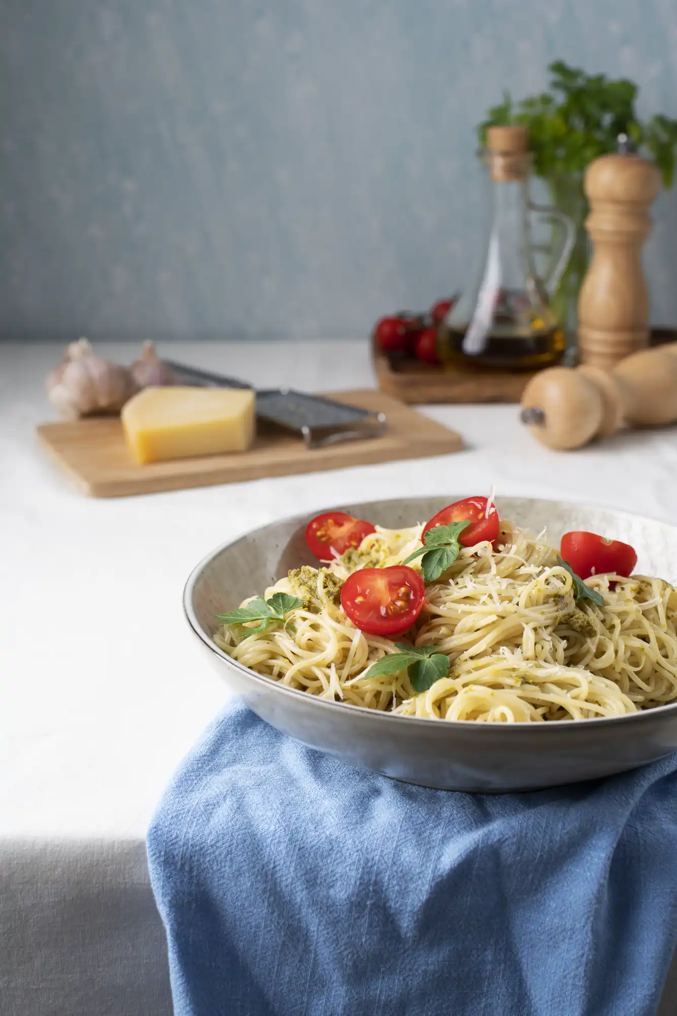 Tanjir italijanske paste s pestom, cherry paradajzom i svježim začinskim biljem, na stolu s rendanim parmezanom i začinima.
