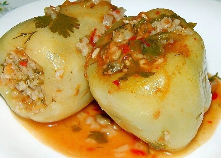 punjene-paprike-sa-rizom Dvije posne punjene paprike sa rižom, u paradajz sosu, servirane u tanjiru.