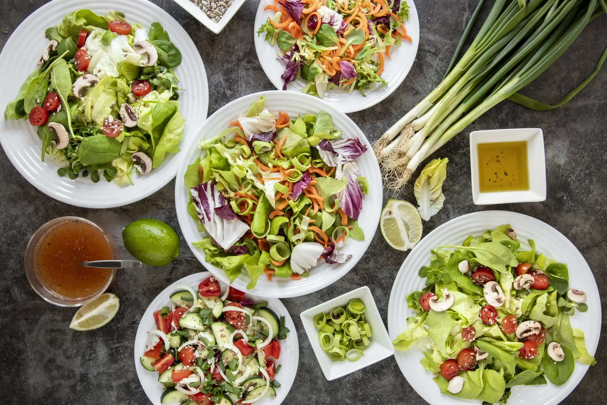 Više različitih salata na tanjirima sa svježim povrćem, maslinovim uljem i limetom