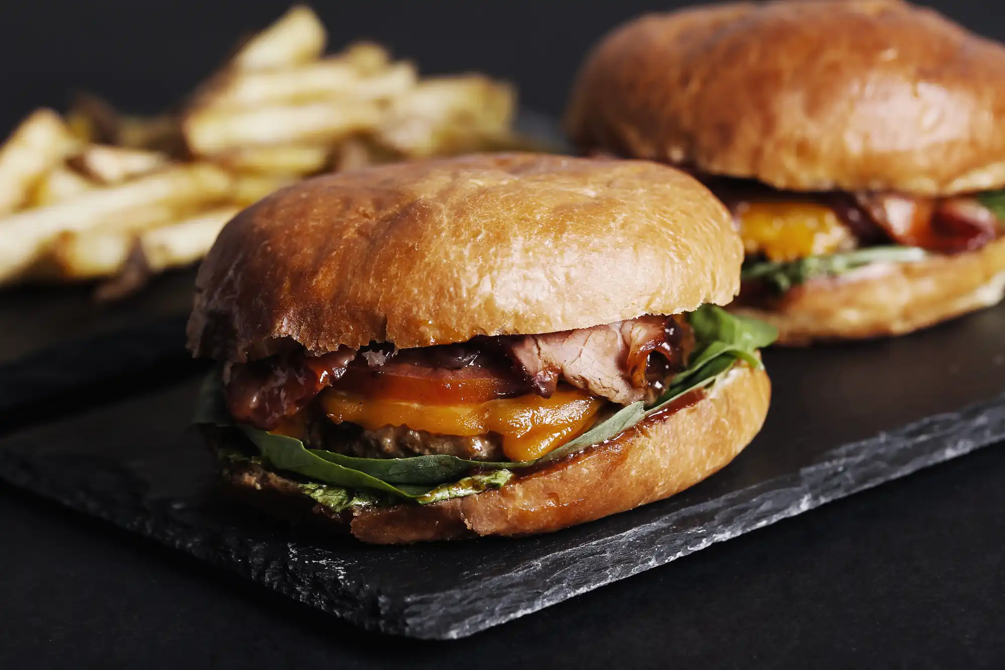 Sočan burger sa sirom, paradajzom, salatom i pomfritom na crnoj ploči - fast food.
