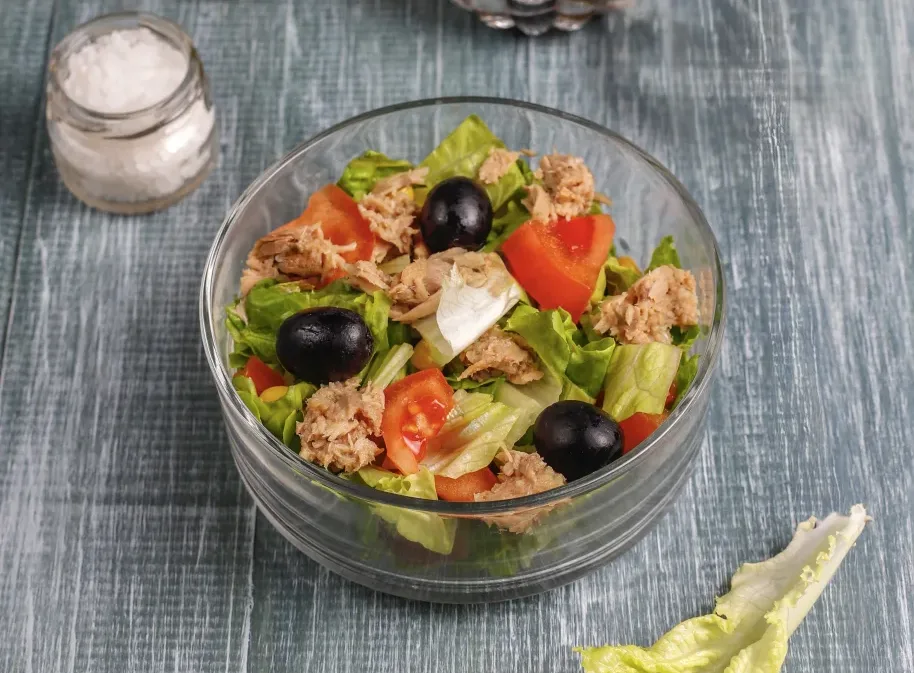 zelena-salata-tunjevina Zelena salata sa tunjevinom, uz dodatak paradajza i crnih maslina, servirana u providnoj činiji.