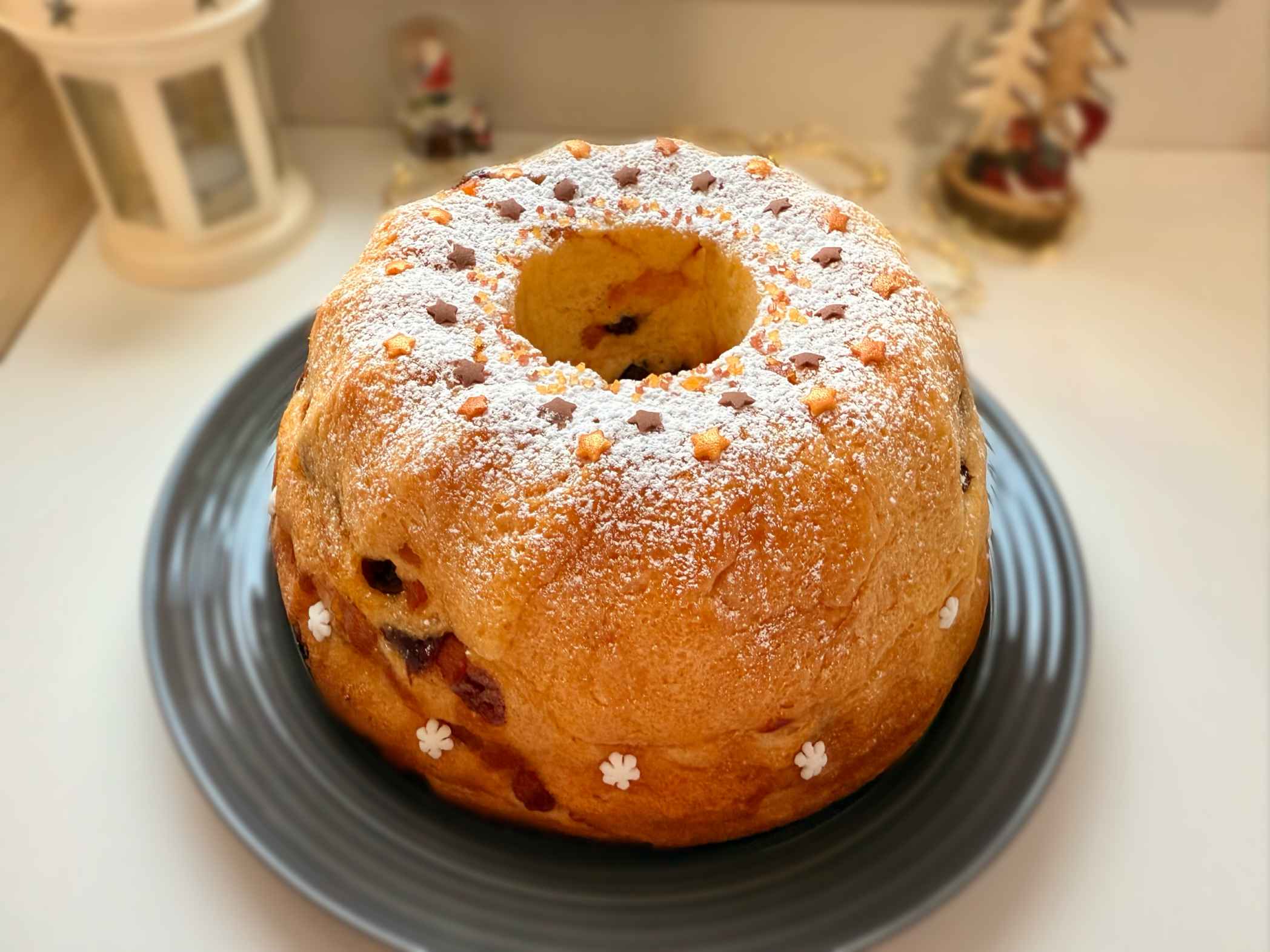 Kuglof sa suhim voćem i citrusima, sočan i sa aromom ruma, serviran na tanjiru, posut šećerom u prahu.