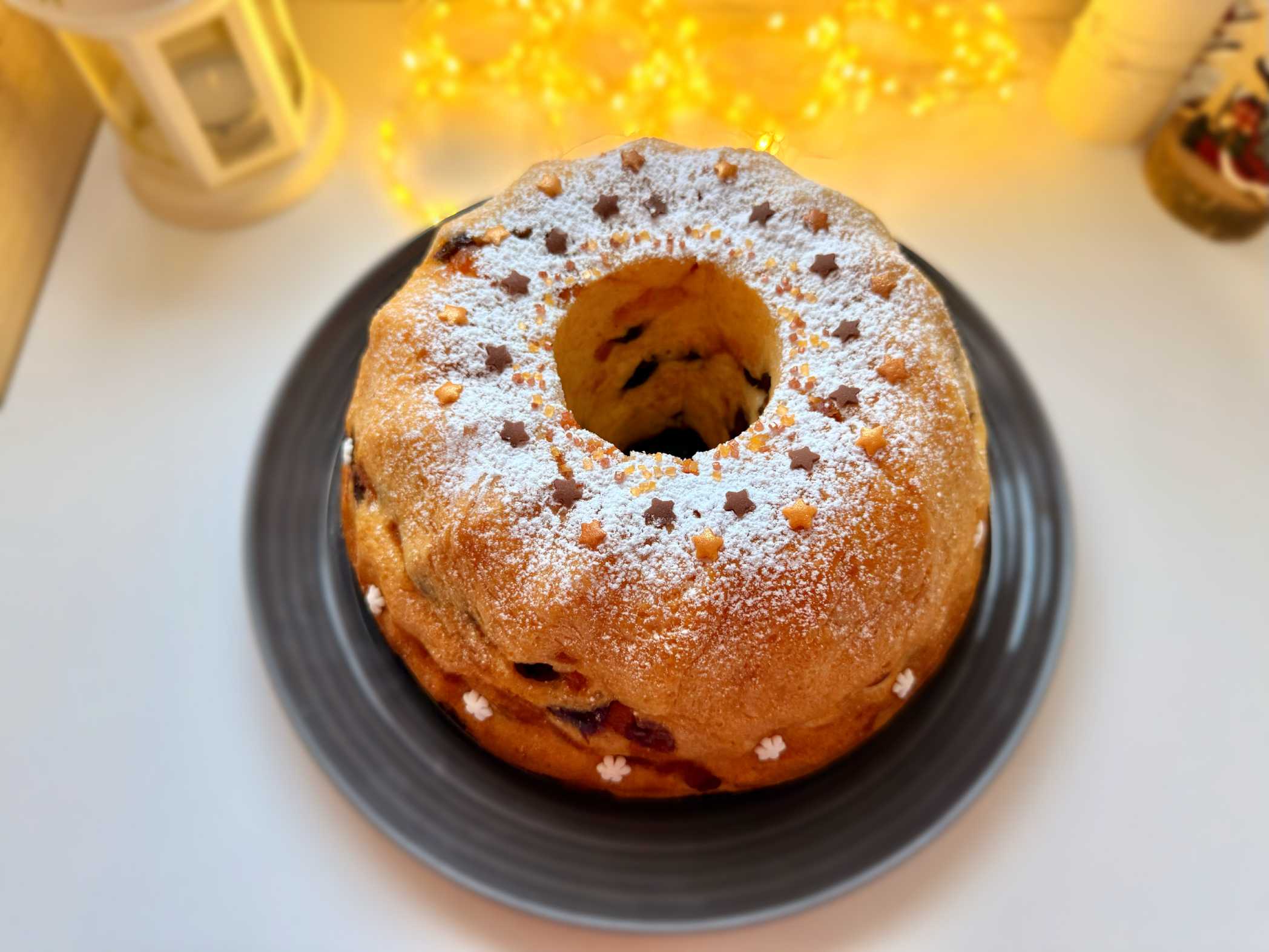 Kuglof sa suhim voćem i citrusima, sočan i sa aromom ruma, serviran na tanjiru, posut šećerom u prahu.