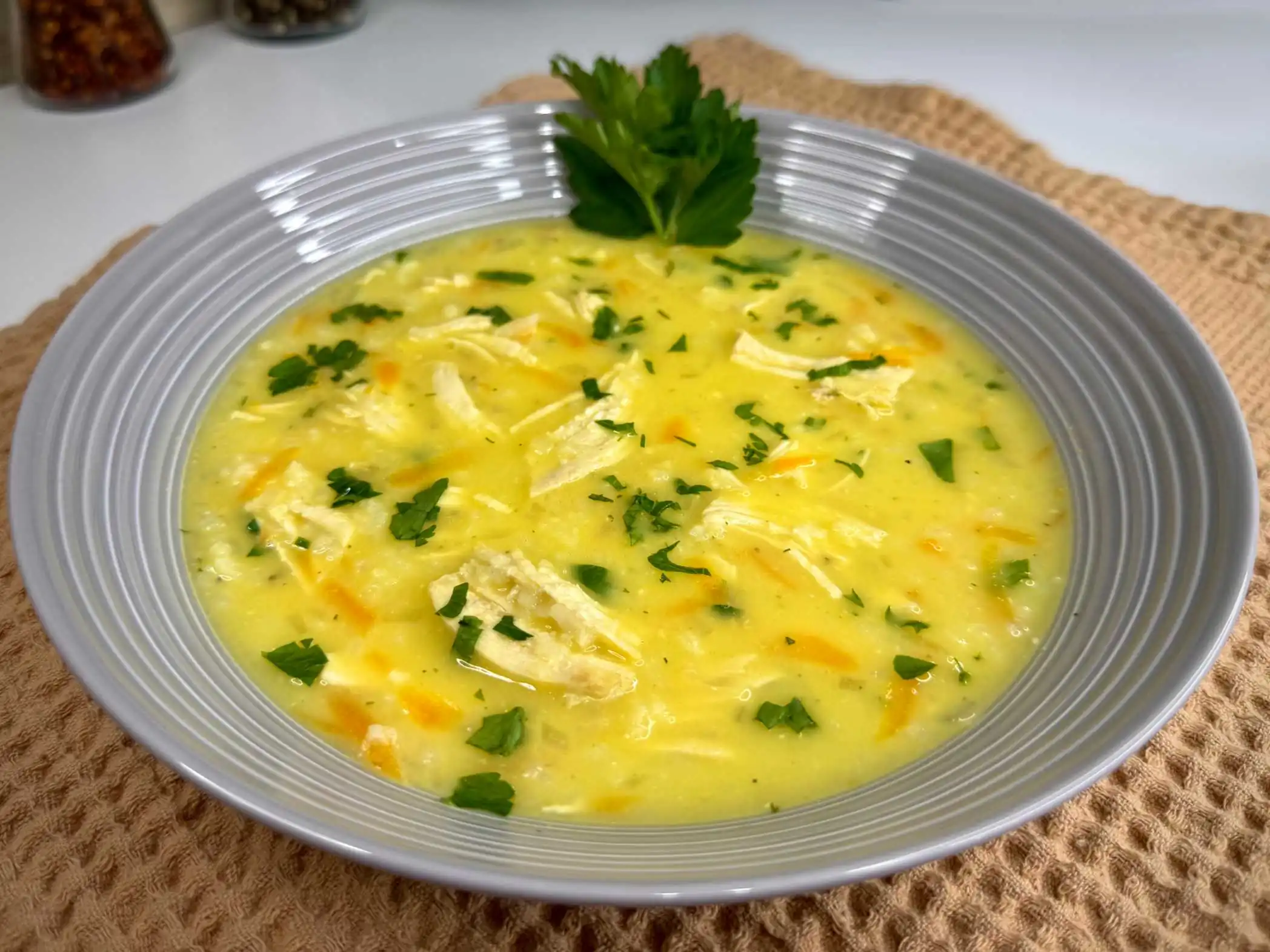 Grčka pileća supa sa limunom i jajima Avgolemono, servirana u tanjiru sa malo peršuna, krpa ispod tanjira za dekoraciju.