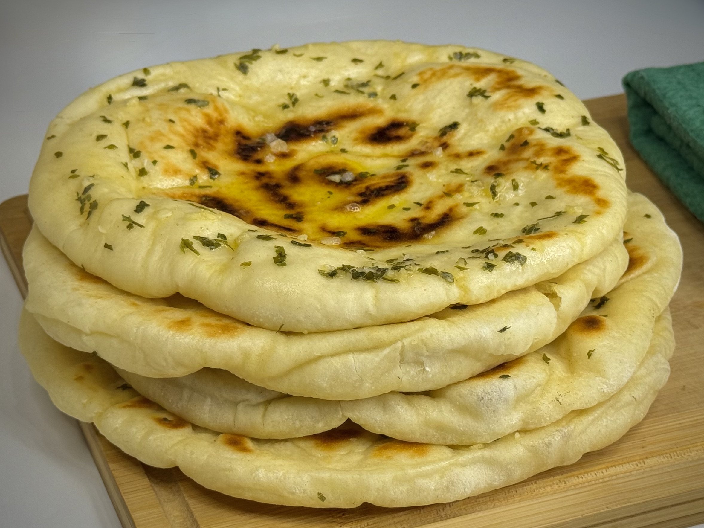 Indijske naan lepinje sa premazom od maslaca, bijelog luka i začina, naslagane jedna na drugu, na drvenoj dasci.